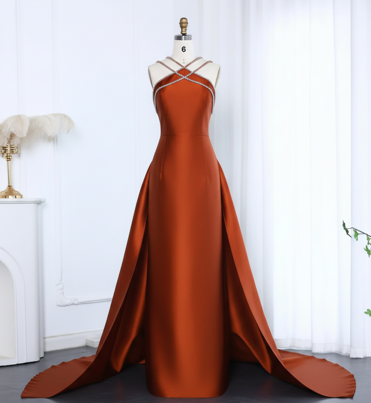 Rust-colored satin evening gown with a crystal-beaded halter neckline, trumpet silhouette, and dramatic overskirt train.