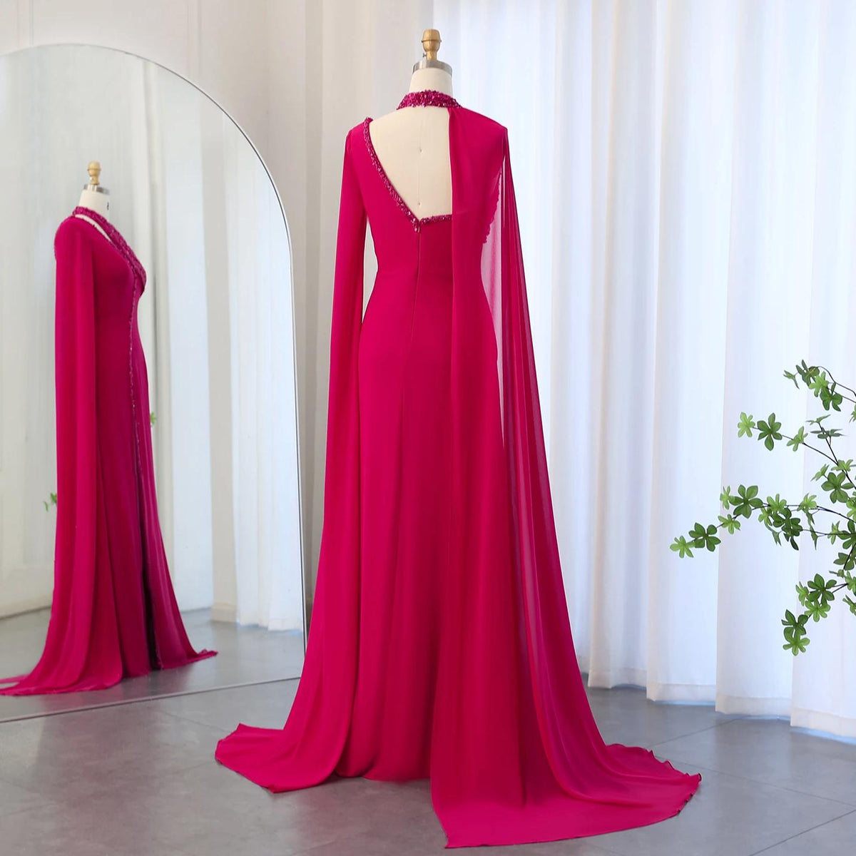 Magenta chiffon floor-length gown with a beaded halter neckline, dramatic cape sleeves, and a sweeping train on a mannequin.