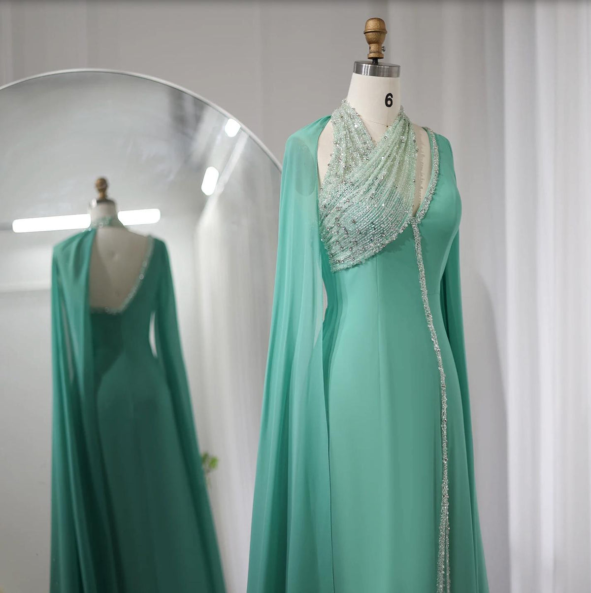 Mint green chiffon Selma gown with beaded halter neckline, cape sleeves, and crystal embellishments on a mannequin.