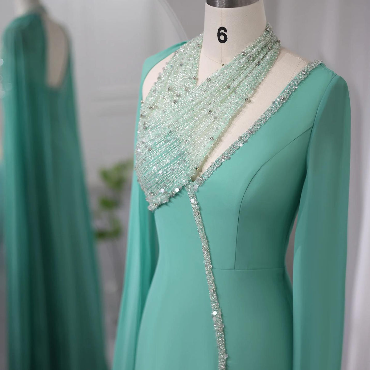 Mint green chiffon Selma gown featuring a beaded halter neckline, crystal embellishments, and dramatic cape sleeves.