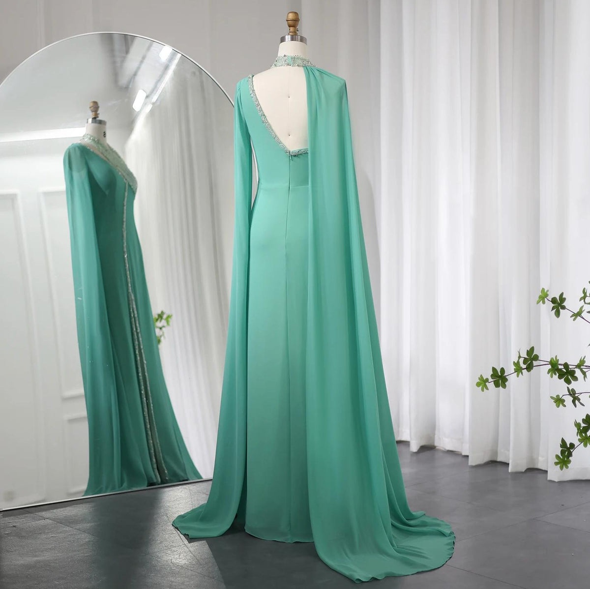 Mint green chiffon Selma gown with a beaded halter neckline, open back, and flowing cape sleeves on a mannequin.