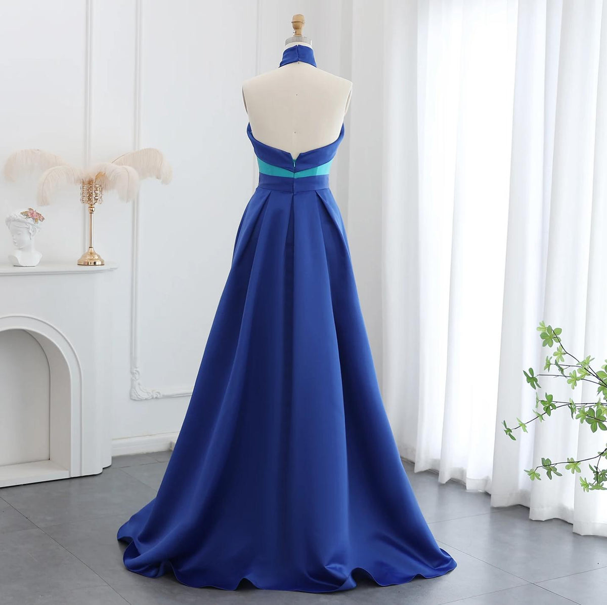Back view of a floor-length royal blue satin A-line gown with a turquoise halter top on a mannequin.