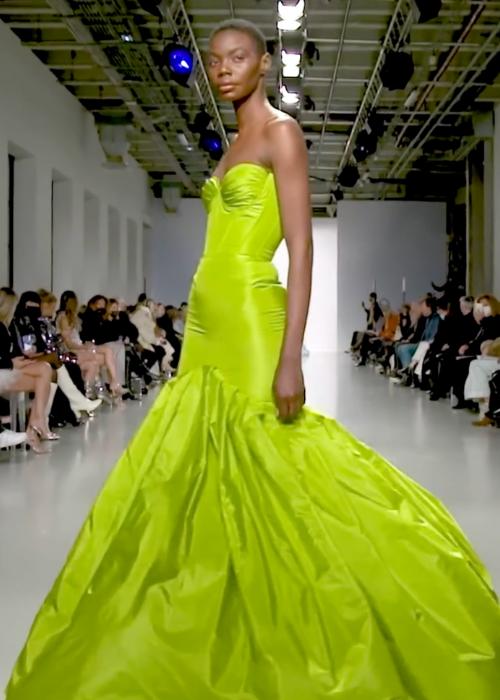 Model wearing a strapless lime green taffeta mermaid gown with dramatic pleated detailing on a runway.