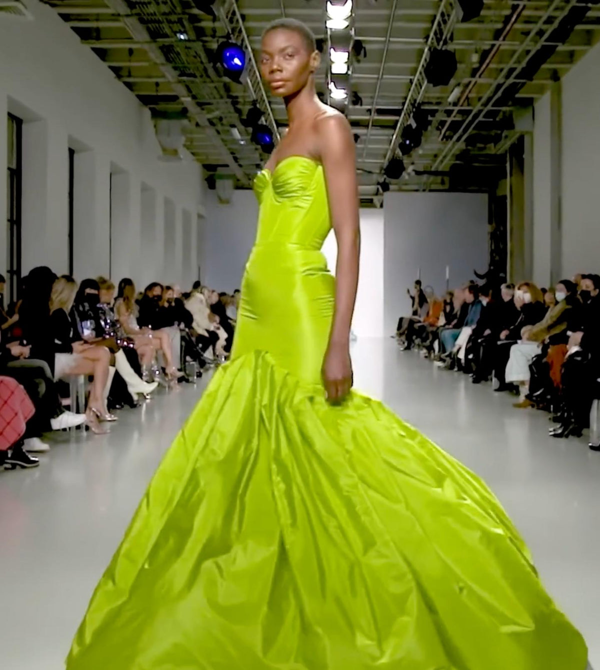 Model in a lime green strapless taffeta mermaid gown with pleated bodice detailing on a fashion runway.