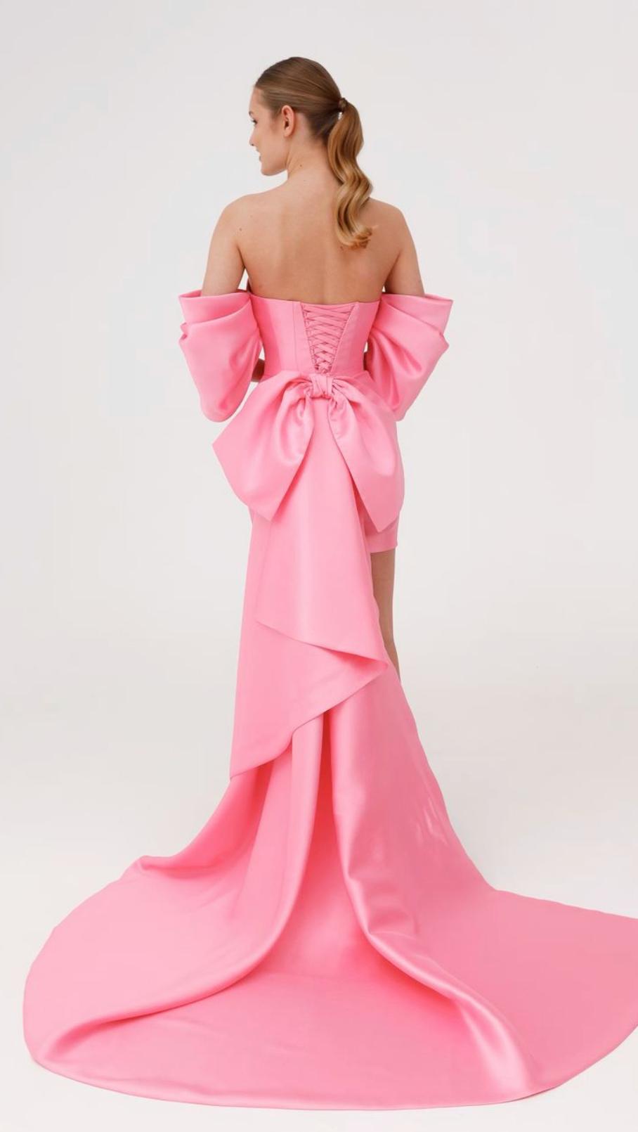 Pink strapless Mikado mini dress with corset back, dramatic bow detail, and a flowing train against a white background.