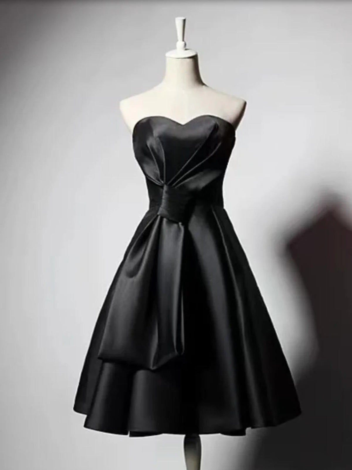 Sleeveless black satin midi dress with a sweetheart neckline, pleated bodice, and flared skirt on a mannequin.