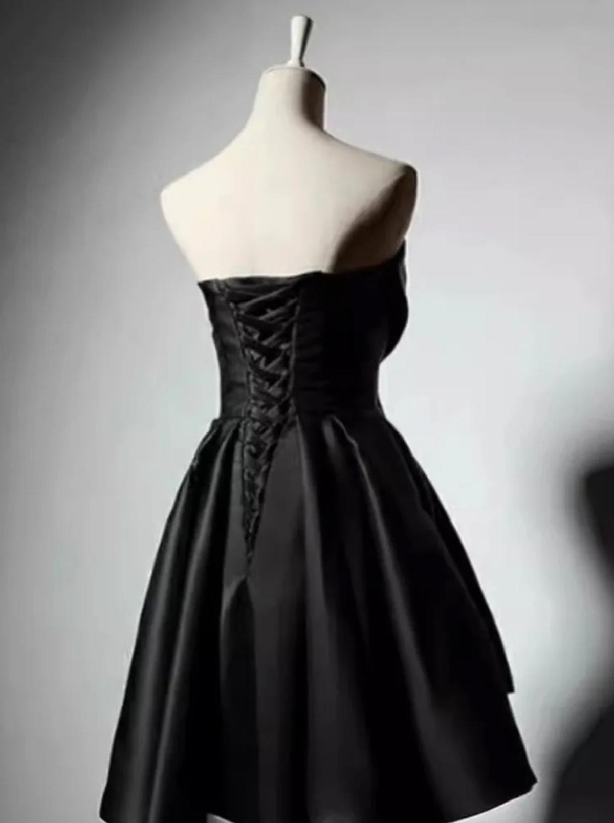 Black satin midi dress with a corset-style lace-up back and pleated skirt on a mannequin.