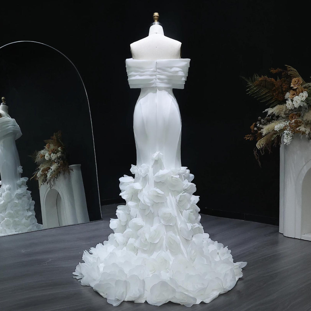 White off-shoulder mermaid gown in satin with 3D floral accents on a floor-length train, displayed on a mannequin.