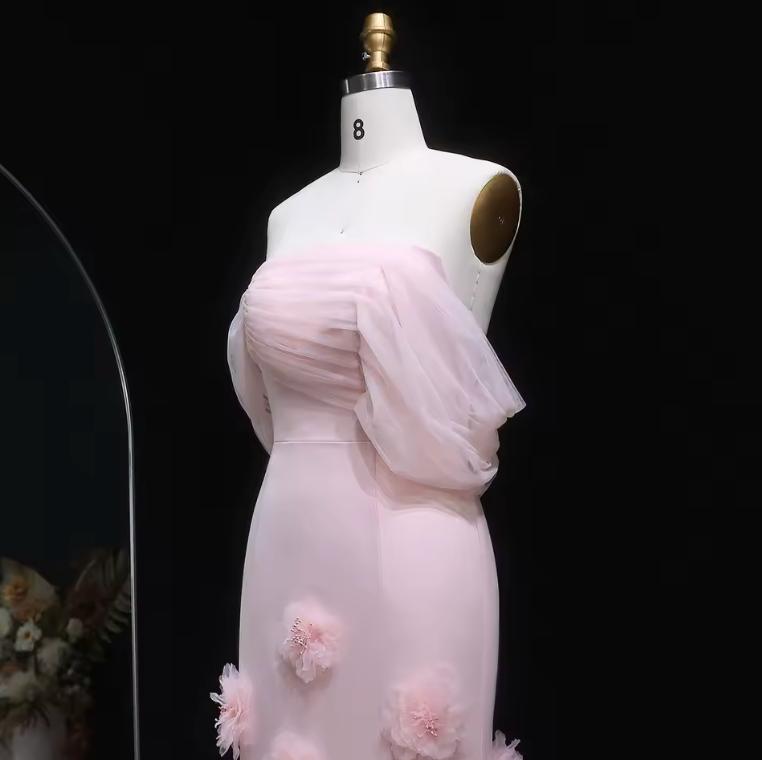 Pink off-shoulder mermaid evening gown in satin with sheer draped sleeves and delicate 3D floral accents on a mannequin.