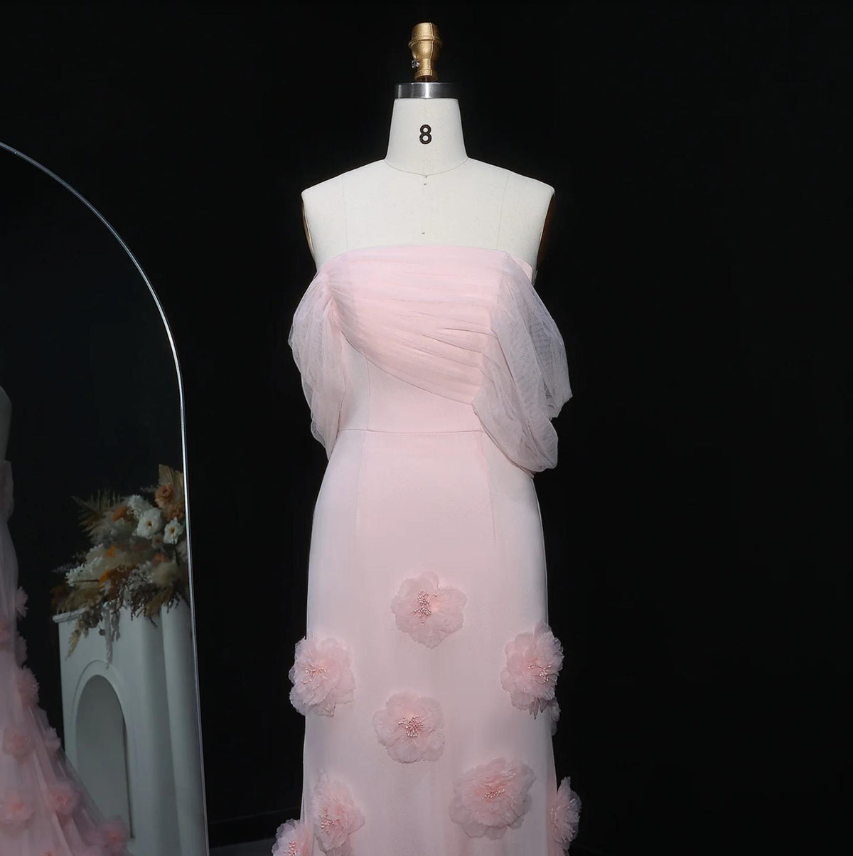 Pink off-shoulder mermaid evening gown in satin with delicate 3D floral accents on a mannequin.