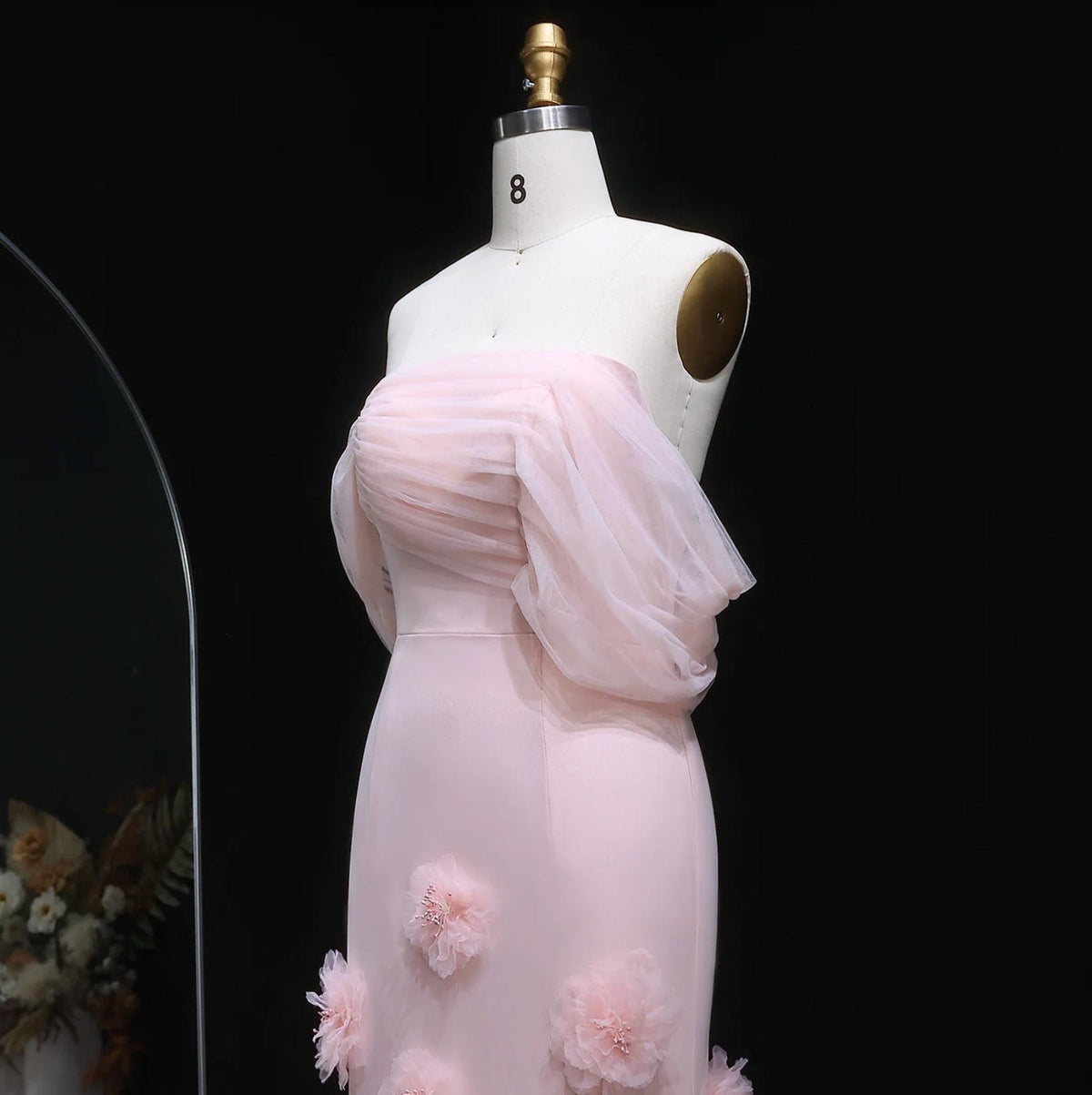 Pink off-shoulder mermaid evening gown with sheer draped sleeves and delicate 3D floral accents on a mannequin.