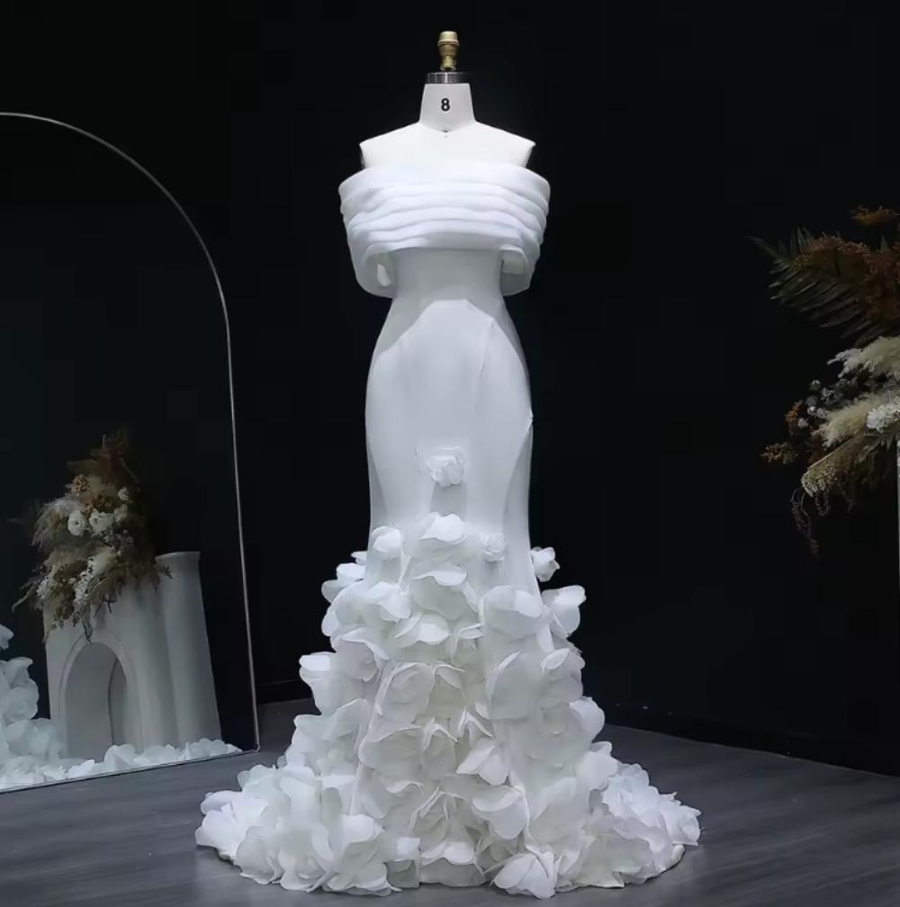 White off-shoulder mermaid evening gown with 3D floral accents on a mannequin against a black background.