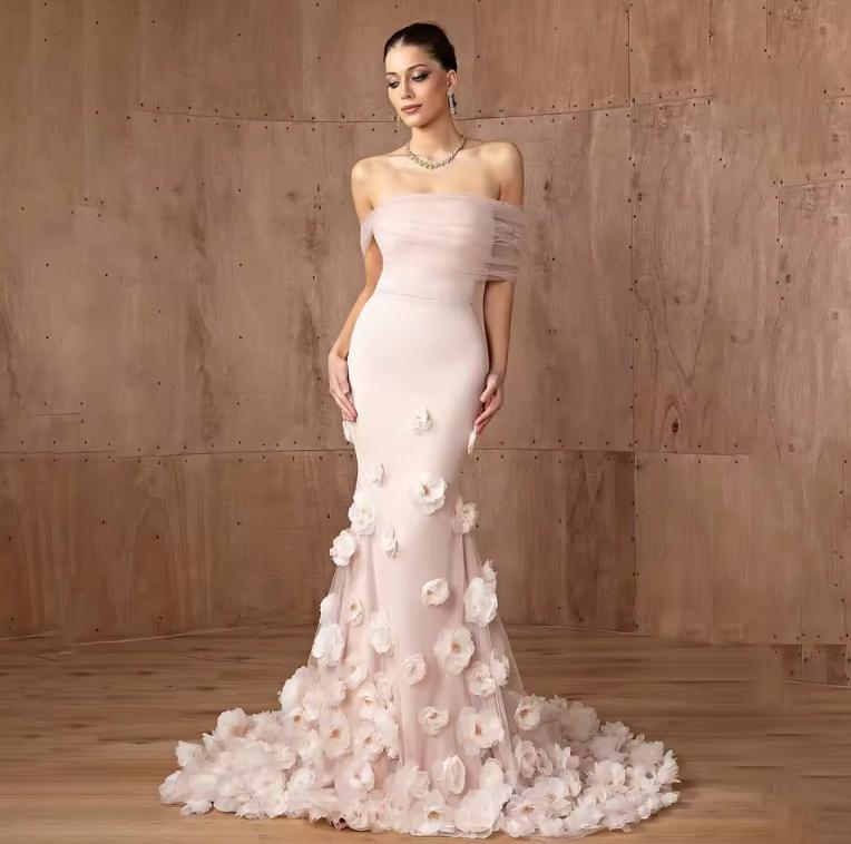 Daring pink off-shoulder mermaid gown in satin with delicate 3D floral accents and a floor-length silhouette.