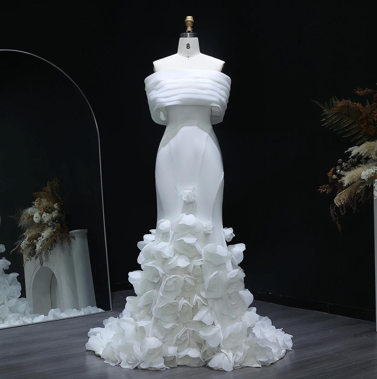 White off-shoulder mermaid gown with 3D floral skirt details and satin fabric on a mannequin.
