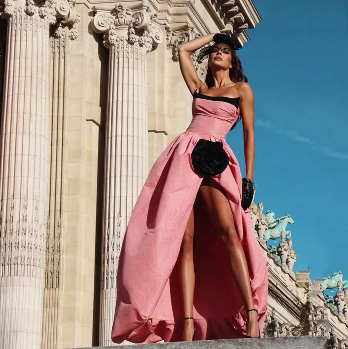 Strapless pink taffeta evening gown with a high slit, voluminous silhouette, and black floral accent detail.