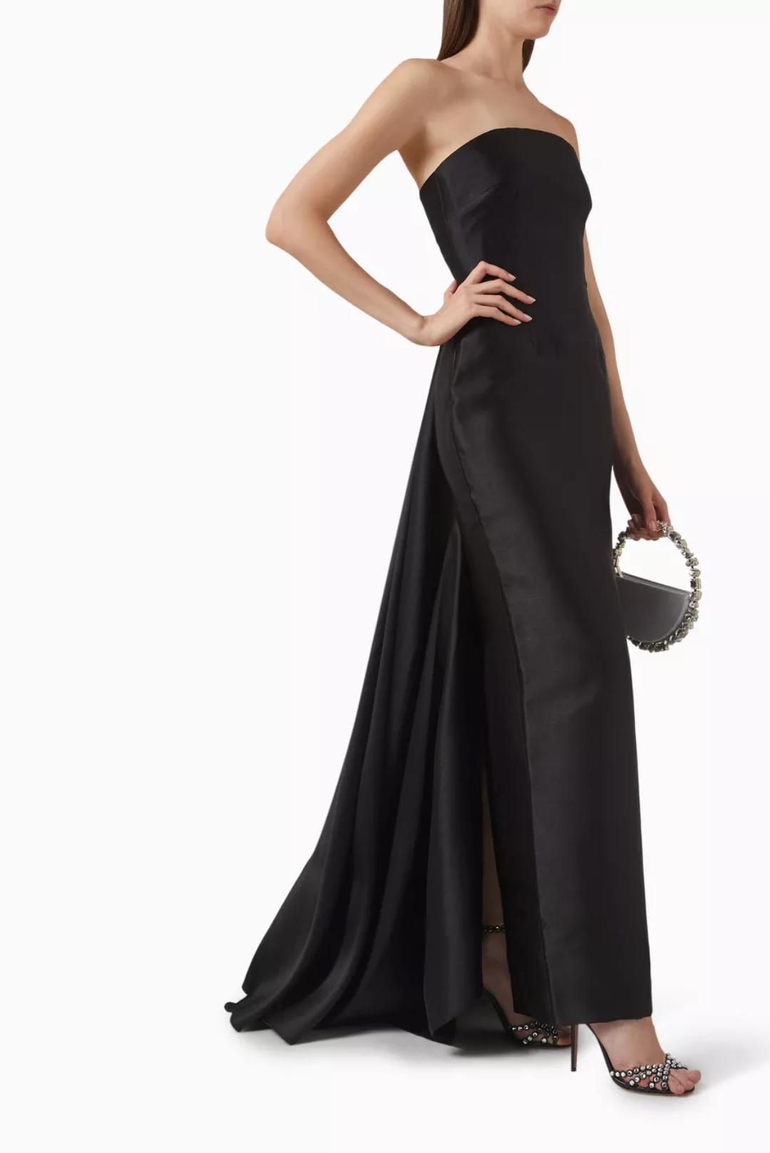 Strapless black satin floor-length gown with a detachable train and side slit, styled with a beaded handbag and heels.