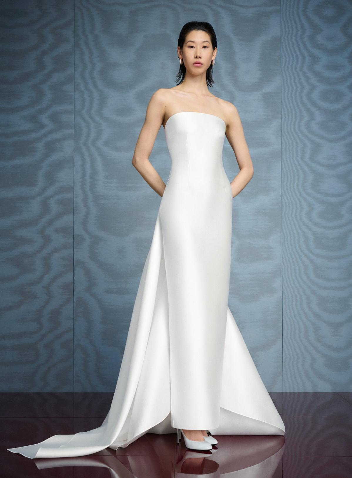 Model wearing a white strapless satin gown with a floor-sweeping detachable train and sleek, minimalist silhouette.