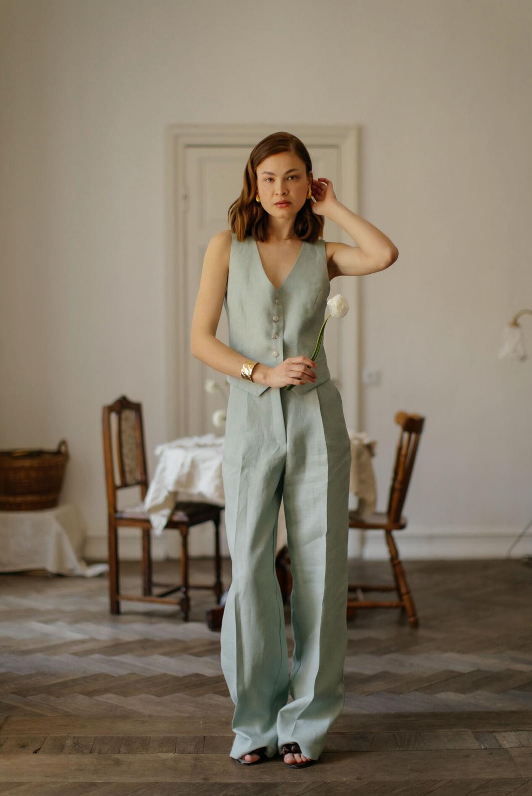 Woman wearing a sage green linen vest and matching high-waisted palazzo pants in a bright, minimalist room.