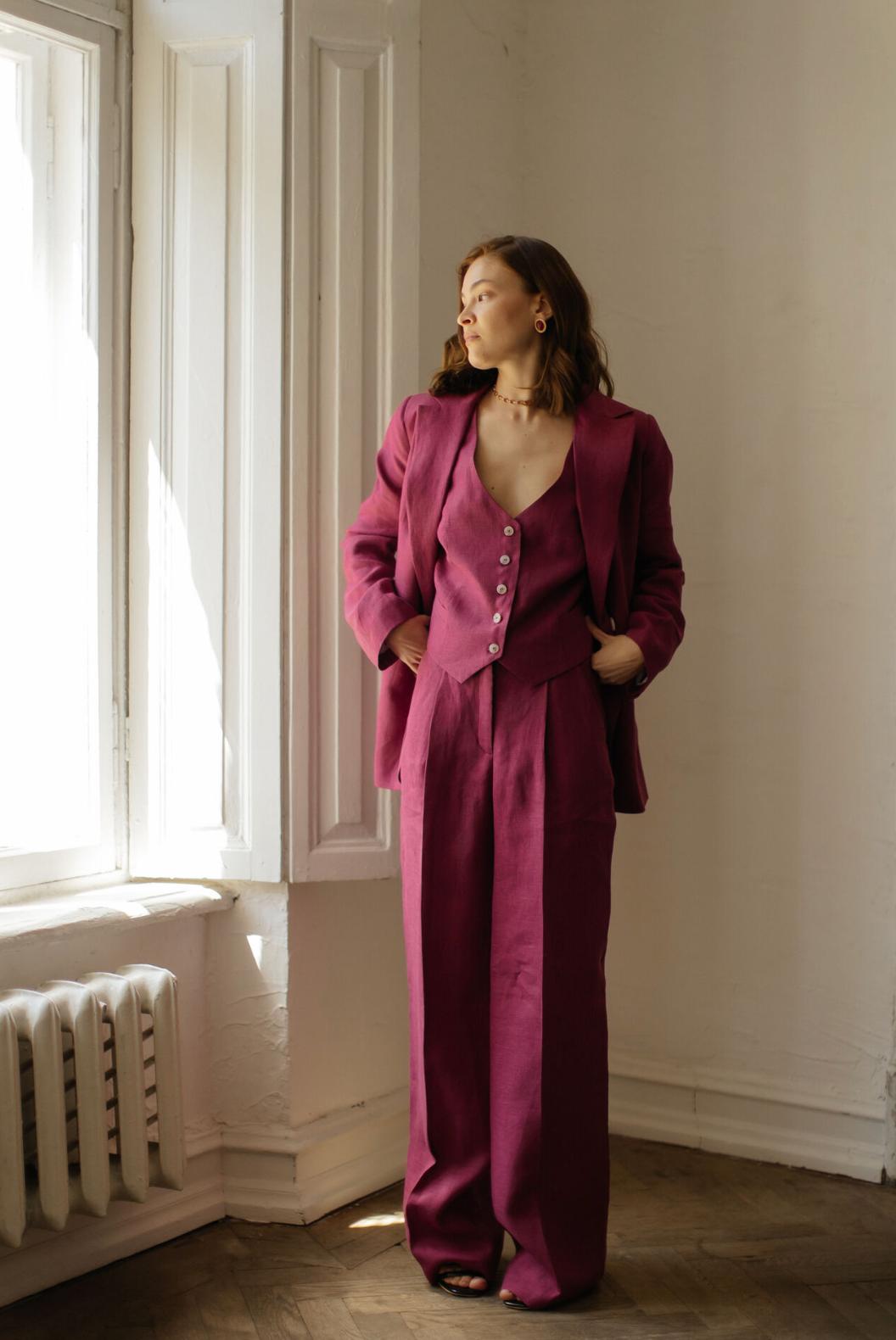 Woman wearing a magenta three-piece linen suit with a tailored jacket, buttoned vest, and flowing palazzo pants.