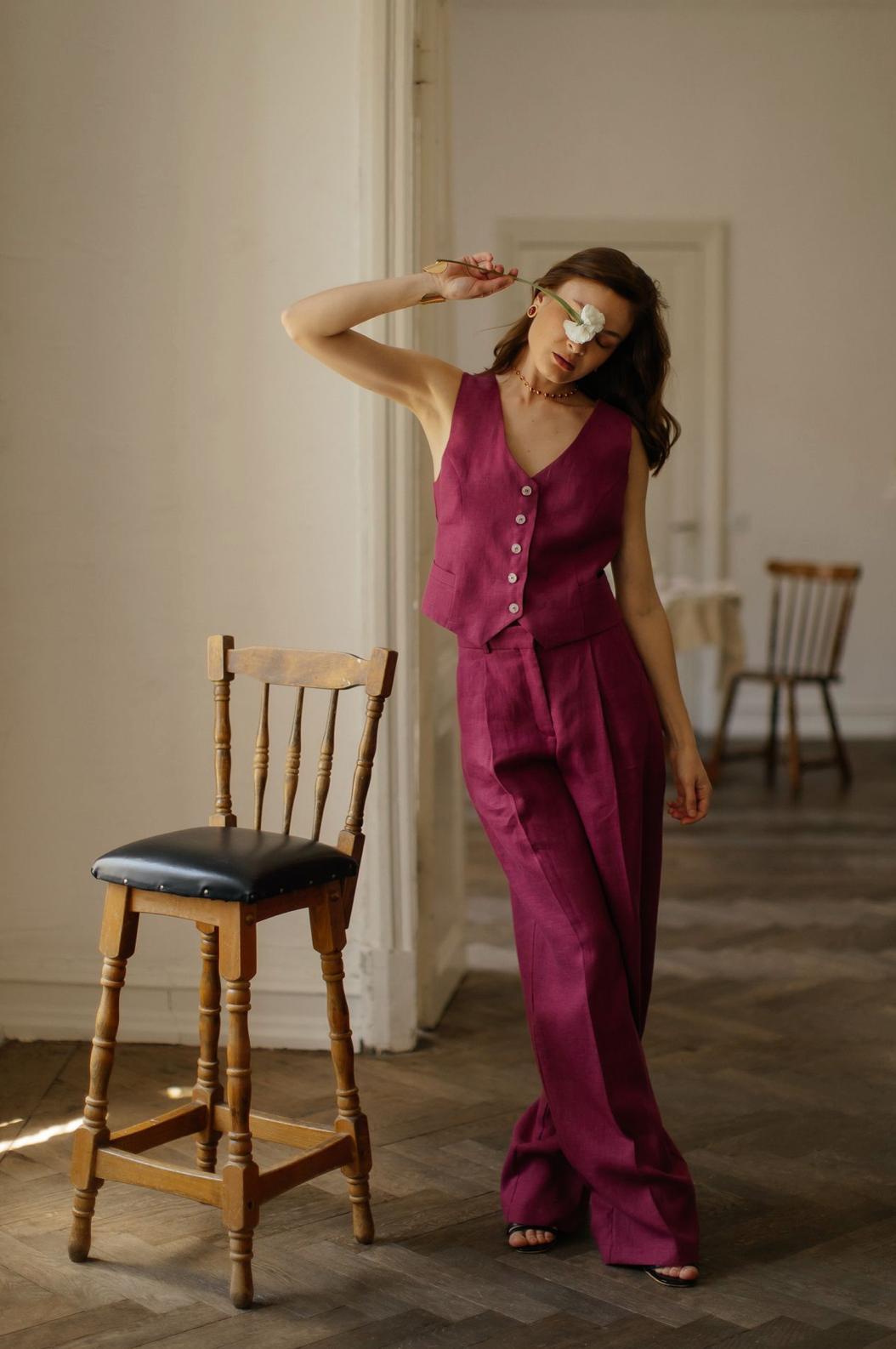 Woman wearing a magenta linen vest and matching palazzo pants, standing elegantly in a sunlit room.