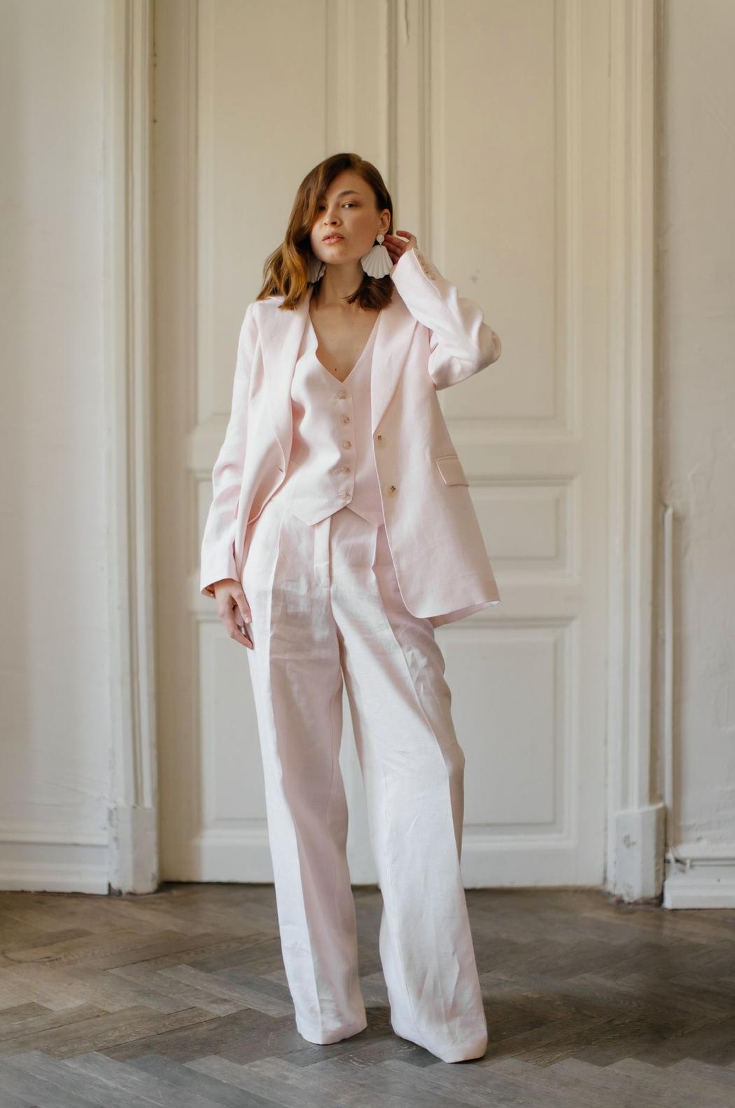 Woman wearing a light pink three-piece linen suit with a tailored jacket, vest, and flowing palazzo pants.