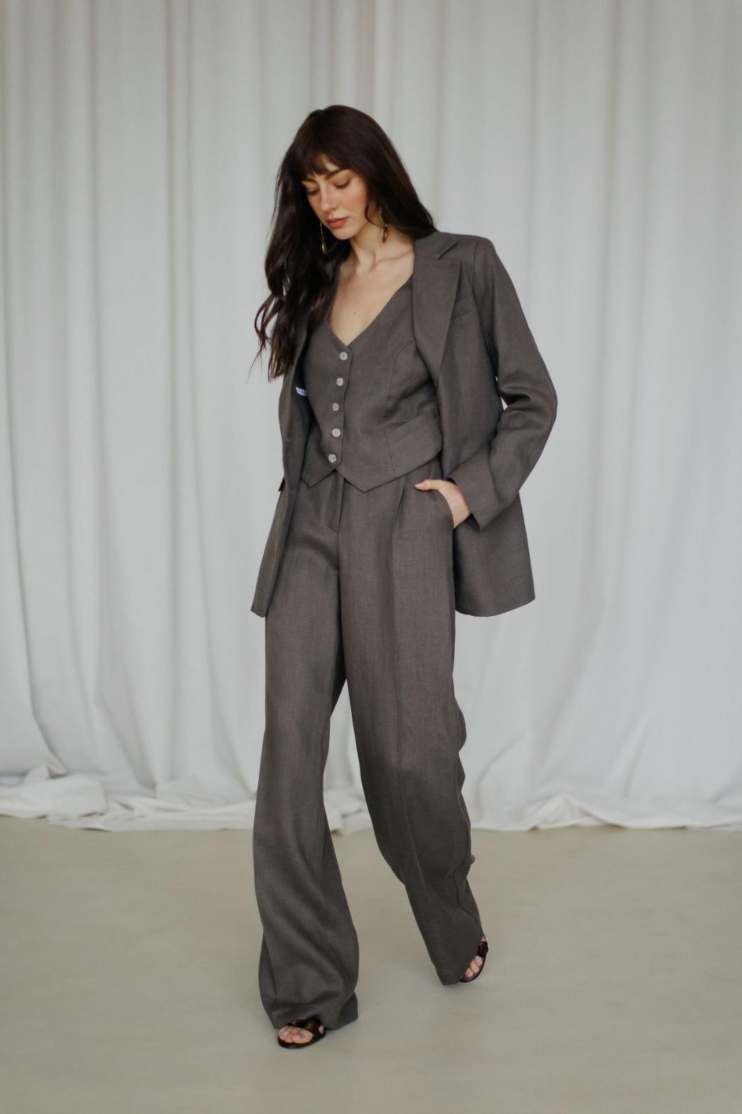 Woman wearing a dark grey three-piece linen suit with a tailored jacket, buttoned vest, and flowing palazzo pants.