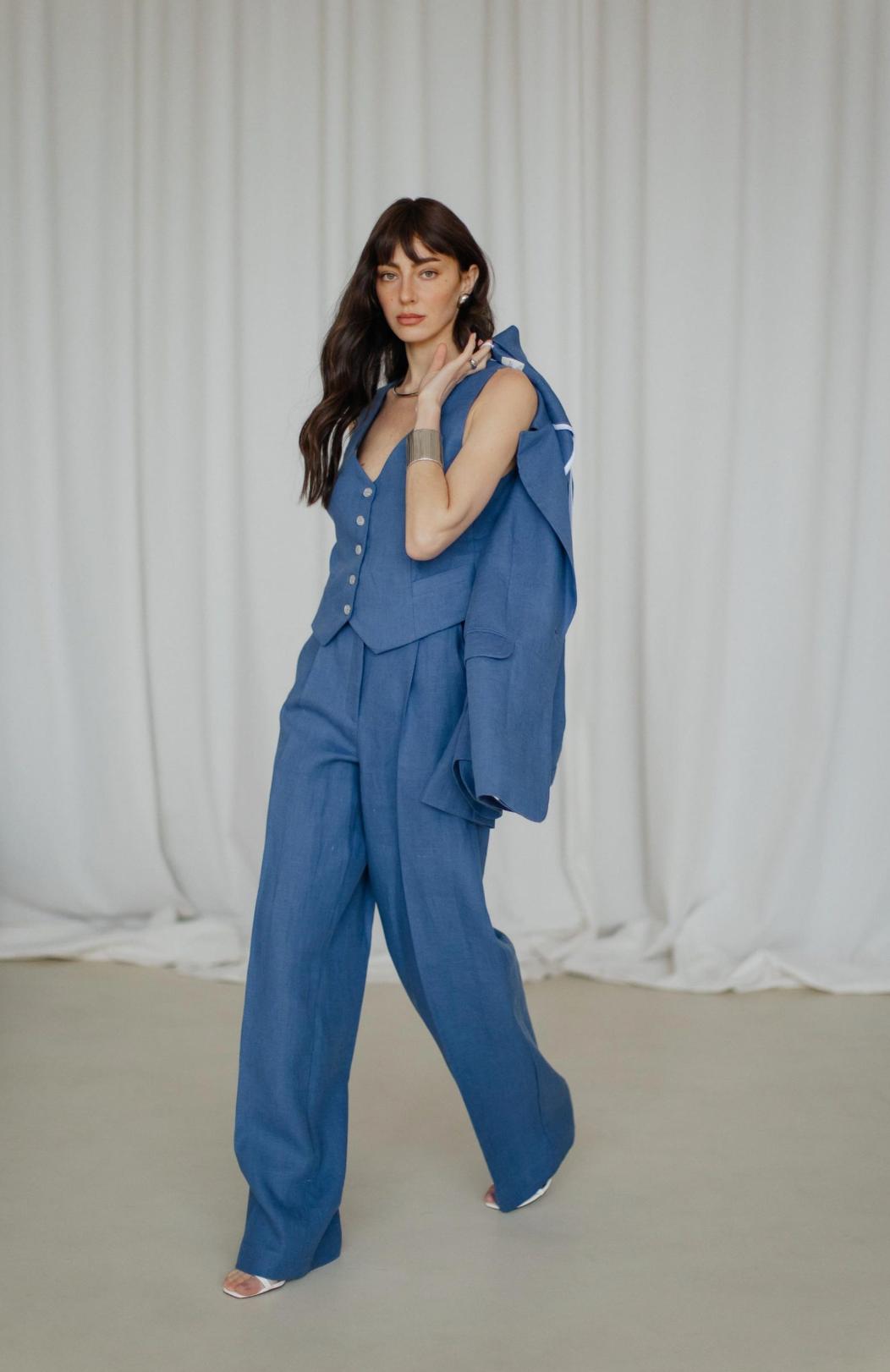 Woman wearing a blue three-piece linen suit with a tailored vest, palazzo pants, and a jacket draped over her shoulder.