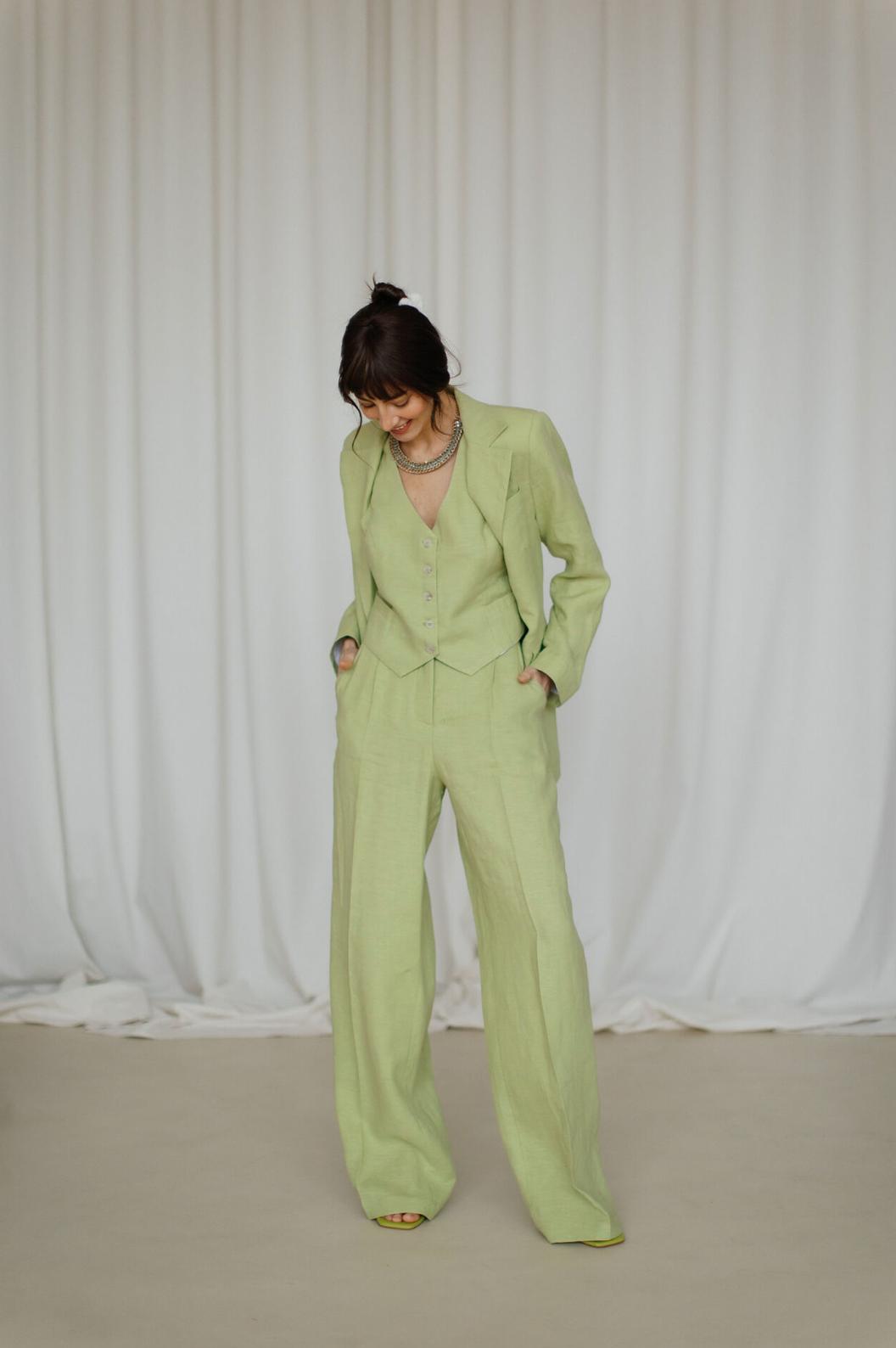 Woman wearing a light green three-piece linen suit with a tailored jacket, button-up vest, and flowing palazzo pants.