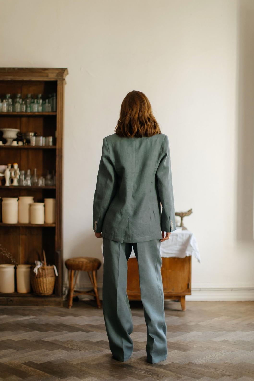 Woman wearing a sage green three-piece linen suit with a tailored jacket and flowing palazzo pants.