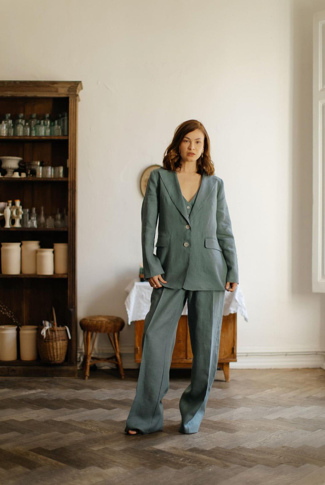 Woman wearing a sage green three-piece linen suit with a tailored jacket, vest, and flowing palazzo pants.