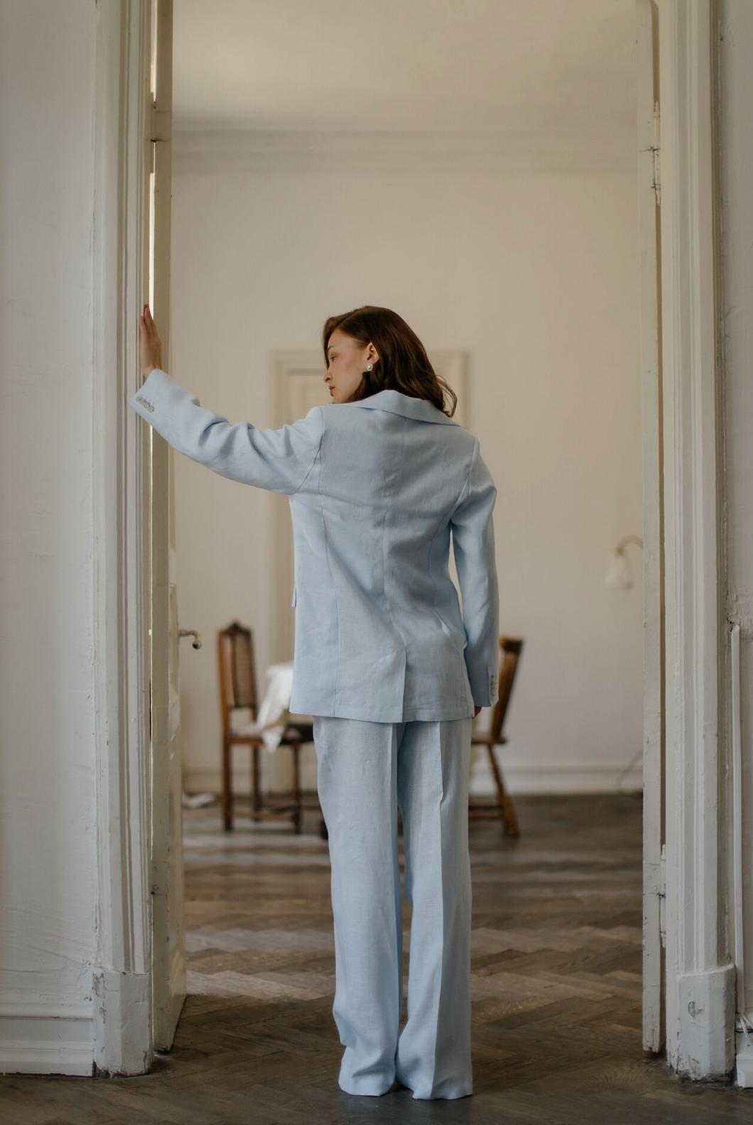 Woman wearing a light blue linen three-piece suit with a tailored jacket and flowing palazzo pants in a bright room.