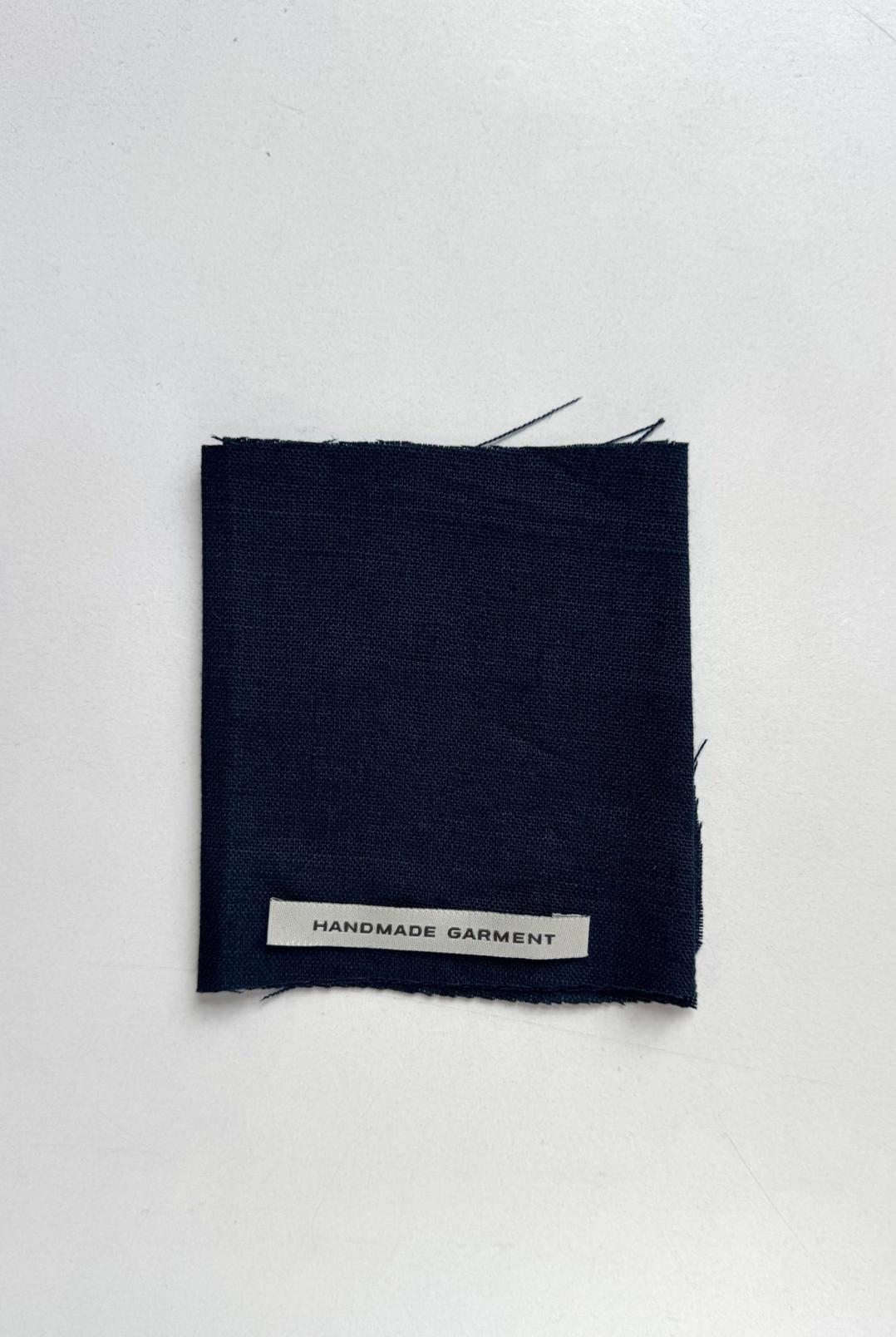 Square swatch of dark navy linen fabric with a white Handmade Garment label attached.