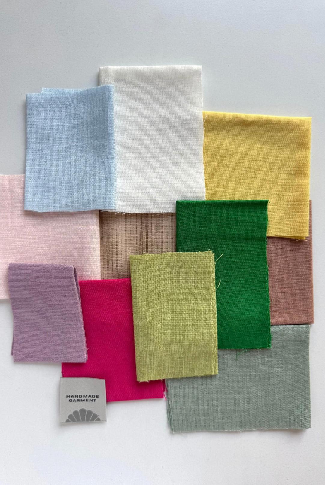 Assorted linen fabric swatches in vibrant and neutral colors for custom Taos suit orders with a handmade garment tag.