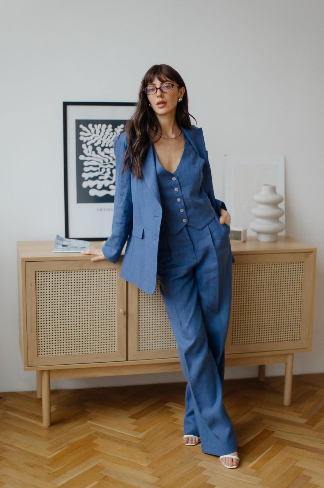 Woman wearing a blue three-piece linen suit with a tailored jacket, buttoned vest, and flowing palazzo pants.