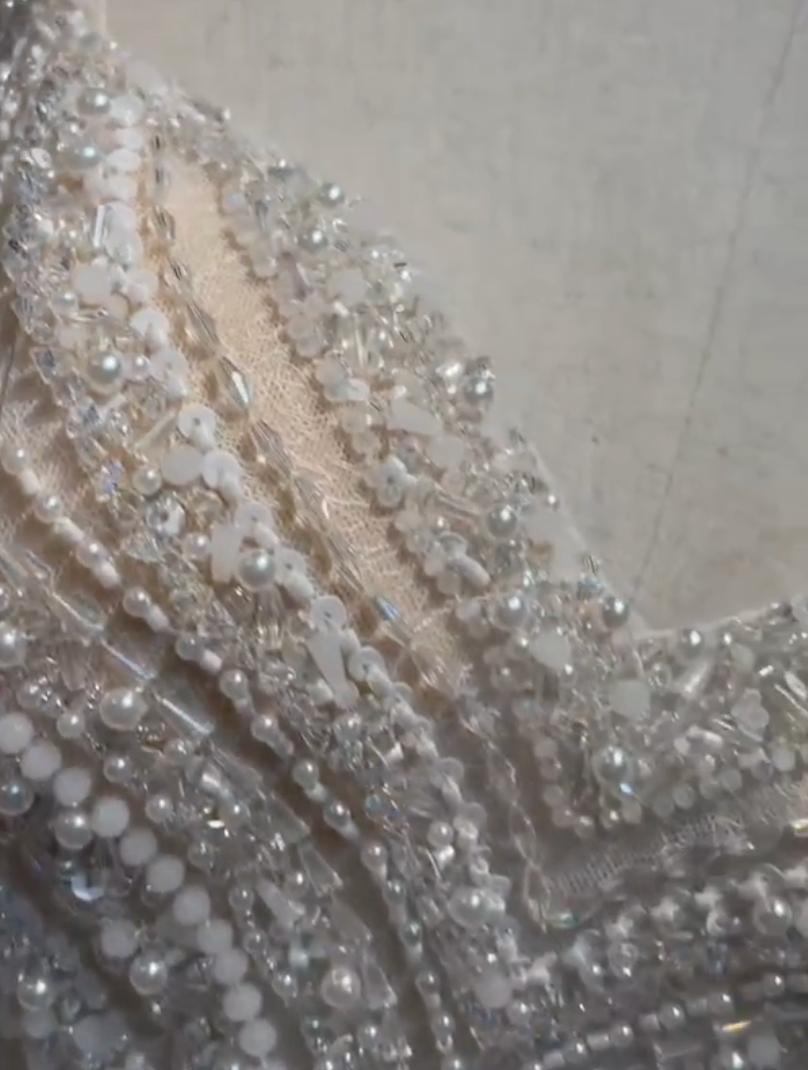 Close-up of a champagne tulle mini dress featuring intricate white beadwork, sequins, and sparkling crystals.