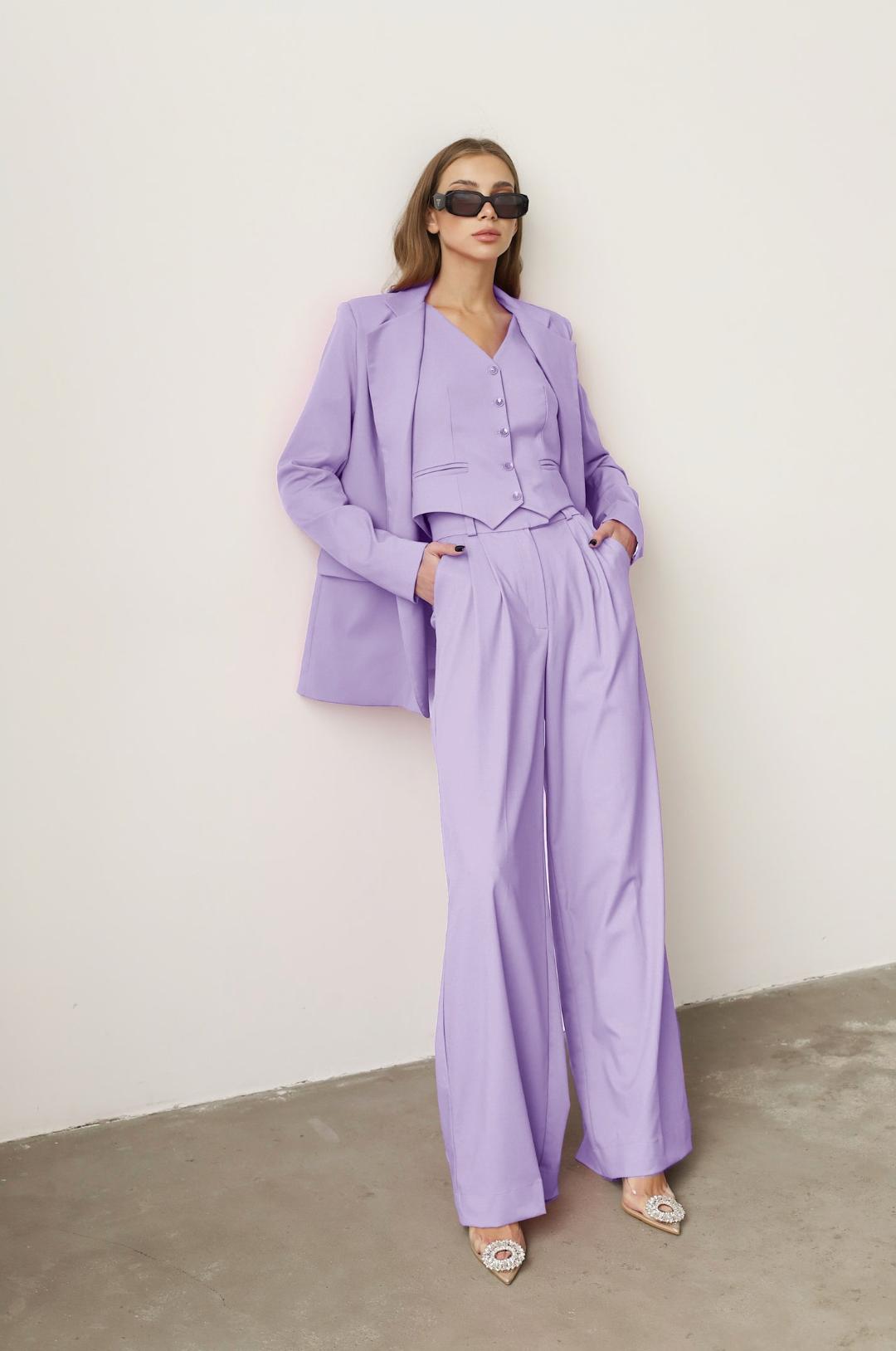 Model wearing a lavender three-piece linen suit with a loose blazer, buttoned vest, and wide-leg trousers.