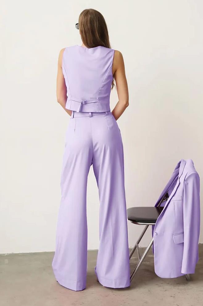 Woman wearing a lavender three-piece linen suit with a vest and wide-leg trousers, with a matching blazer on a chair.