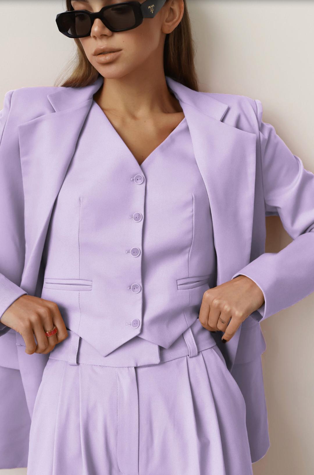 Woman wearing a lavender three-piece linen suit set featuring a loose-fit blazer, buttoned vest, and wide-leg trousers.