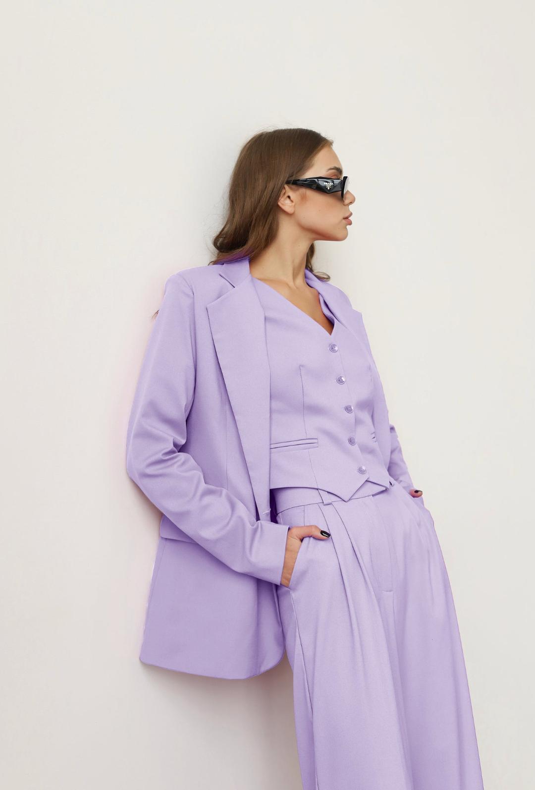 Woman wearing a lavender three-piece linen suit with a loose blazer, buttoned vest, and wide-leg trousers.