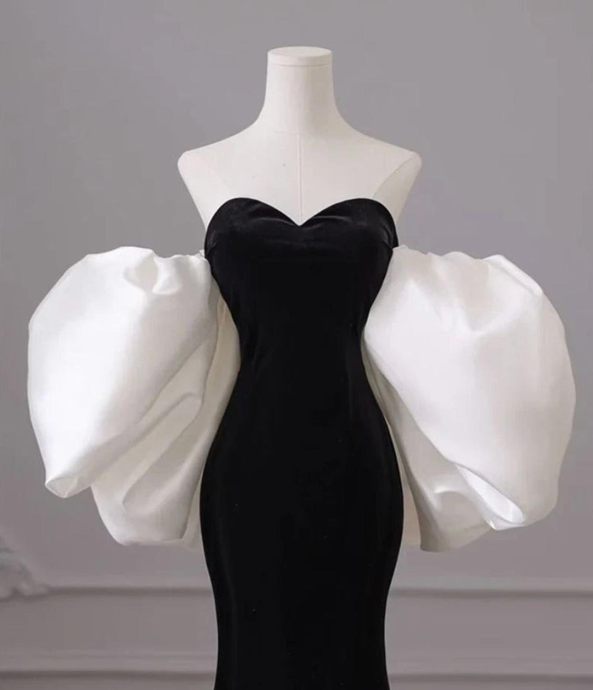 Black velvet strapless mermaid gown with a sweetheart neckline and dramatic white puff sleeves on a mannequin.