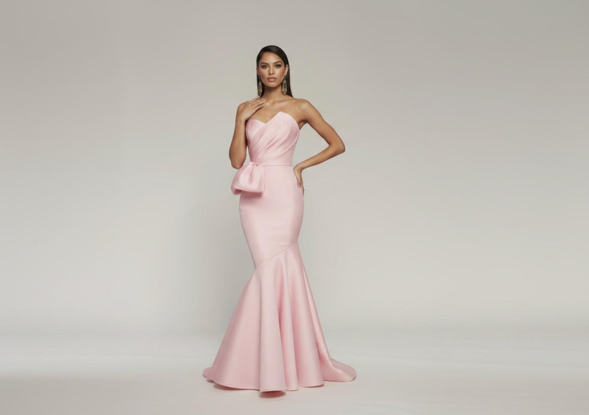 Light pink strapless mermaid gown in pleated satin with a side bow and floor-length flared skirt.