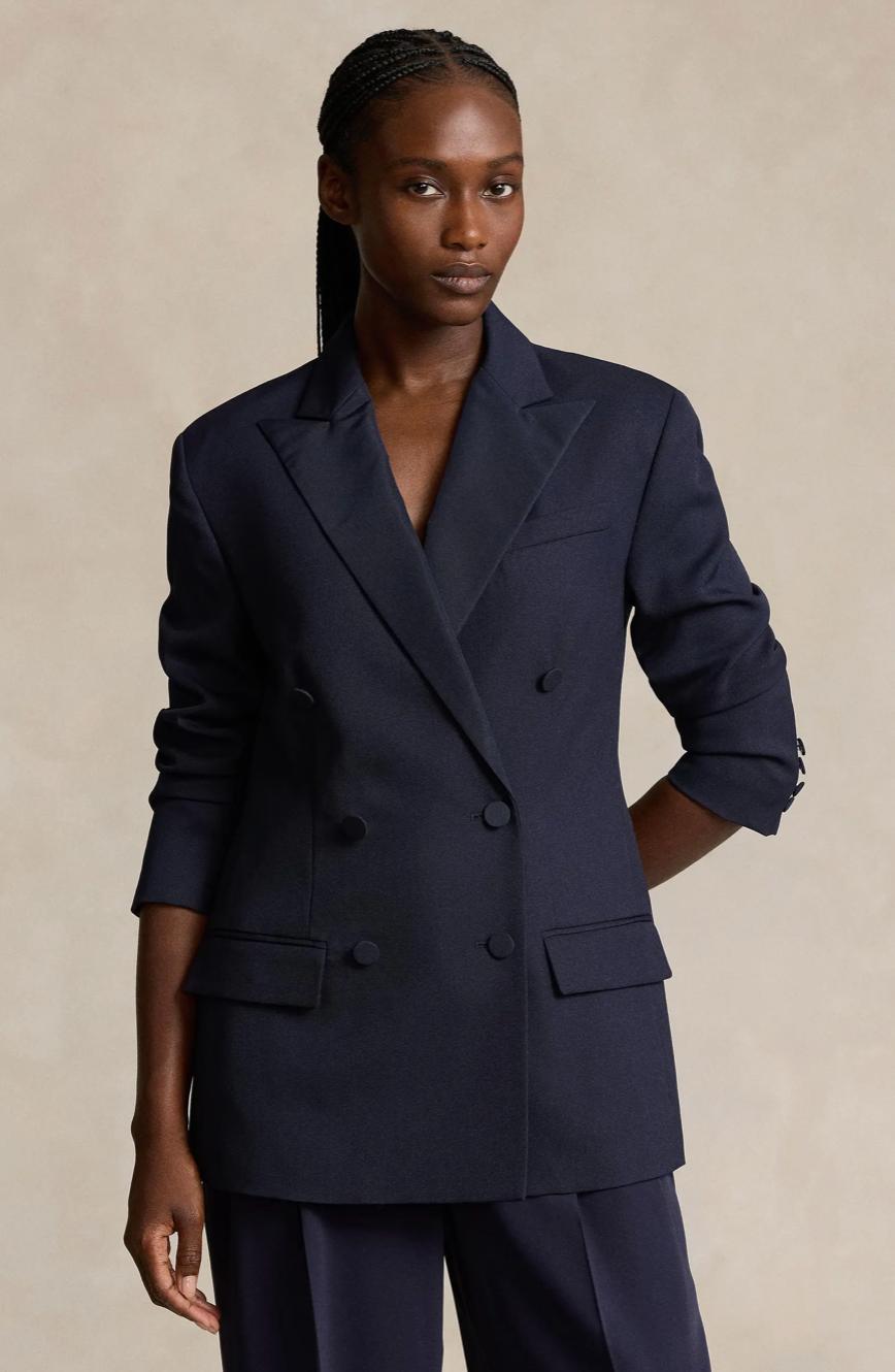 Woman wearing a navy blue double-breasted cotton twill blazer with peak lapels and matching tailored trousers.