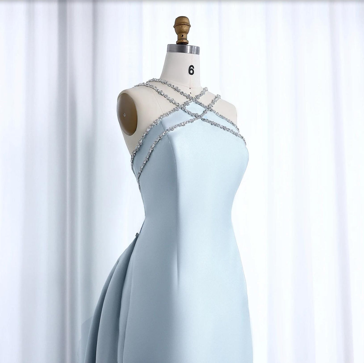 Light blue satin mermaid evening gown with crystal-embellished halter neckline on a dress form.