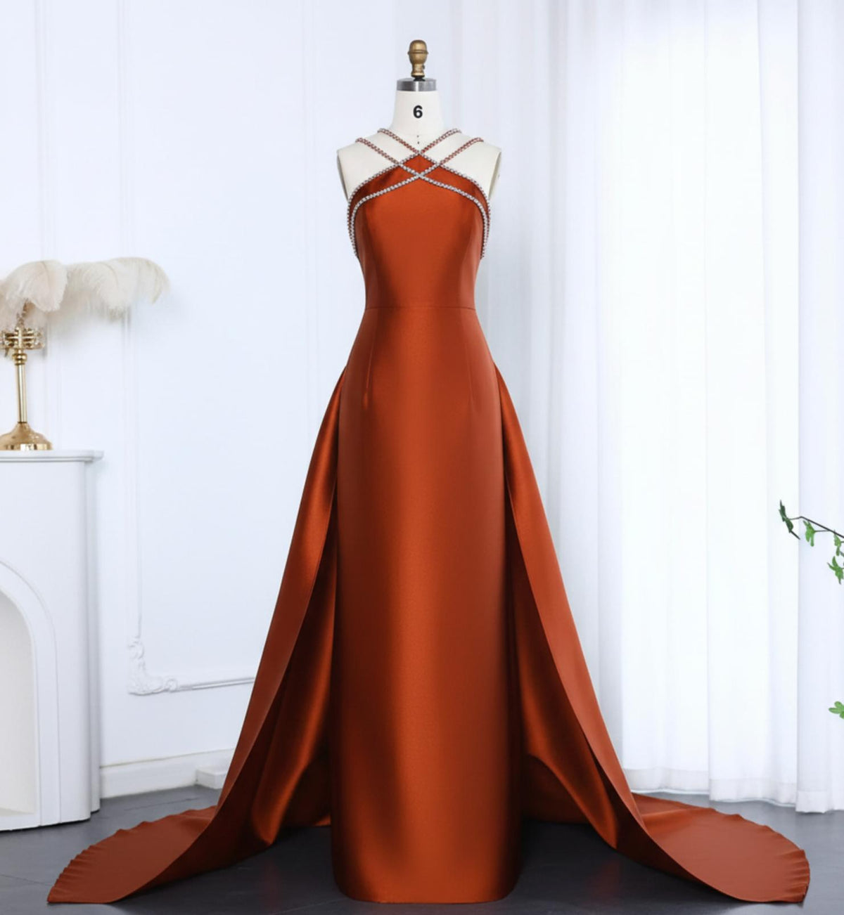 Rust-colored satin evening gown with a crystal-beaded halter neckline, trumpet silhouette, and dramatic overskirt train.