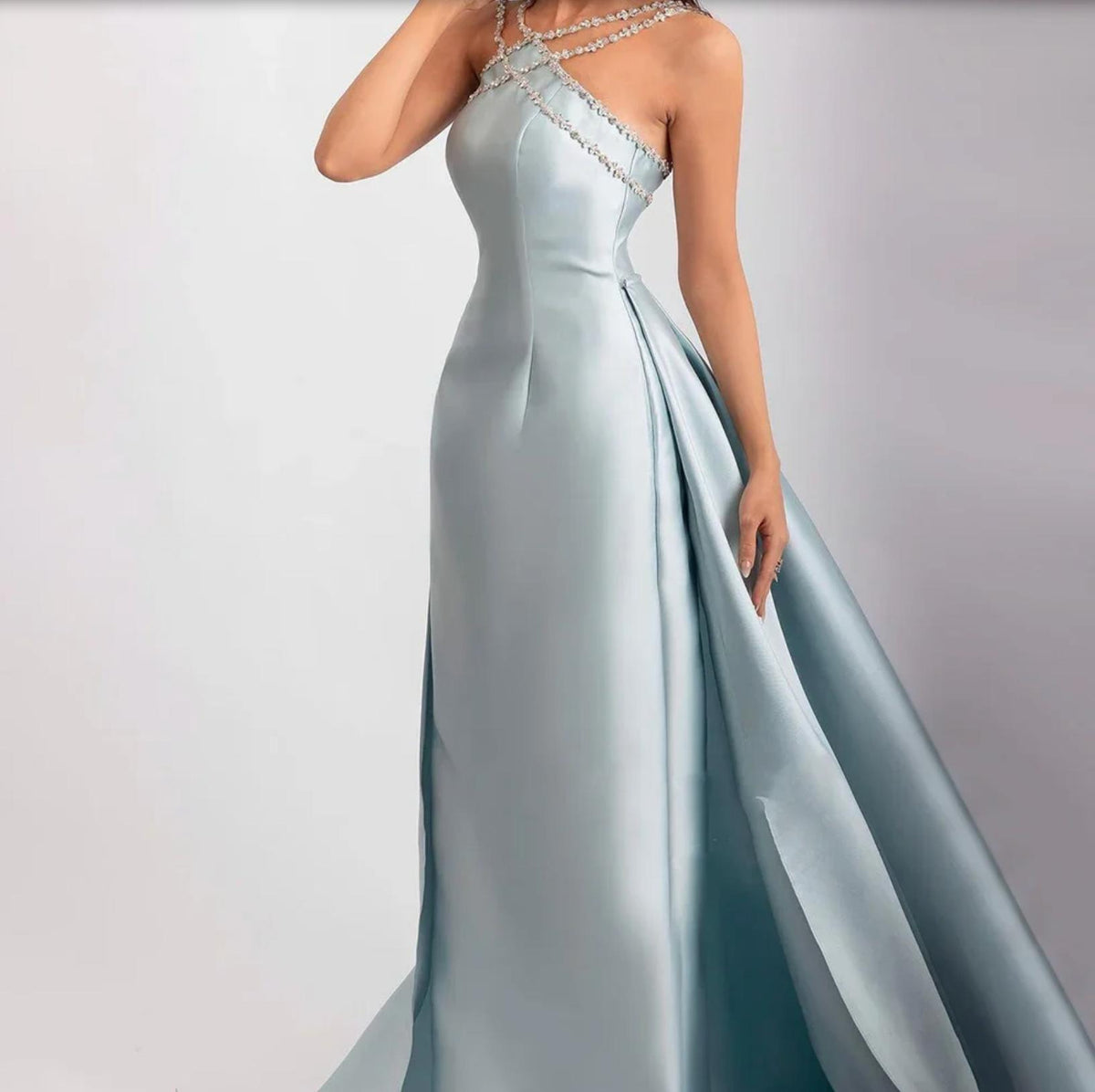 Light blue satin evening gown with a crystal-beaded halter neckline, trumpet silhouette, and dramatic overskirt.