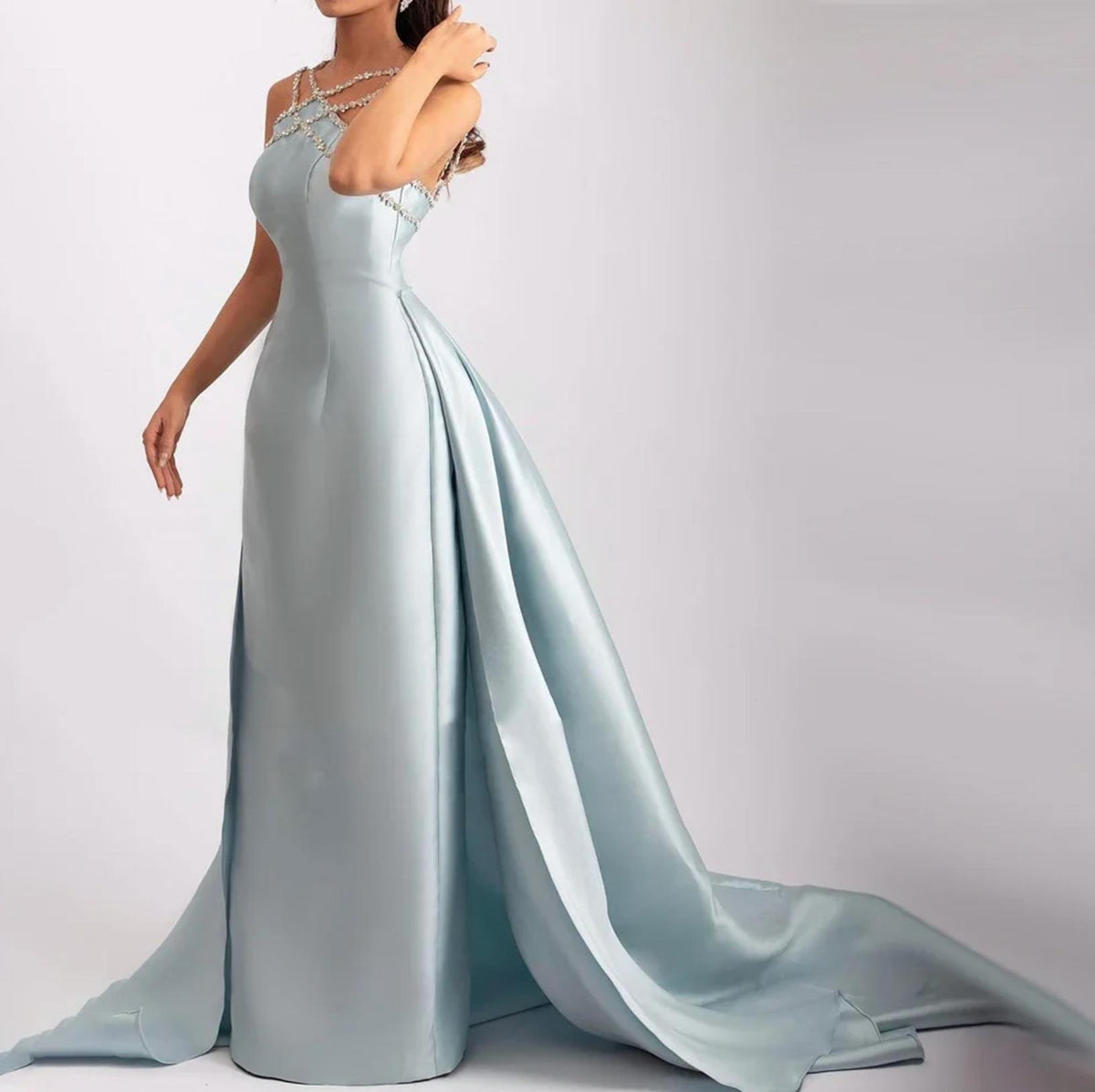 Light blue satin mermaid evening gown with crystal-beaded neckline, sleeveless bodice, and a dramatic detachable overskirt.