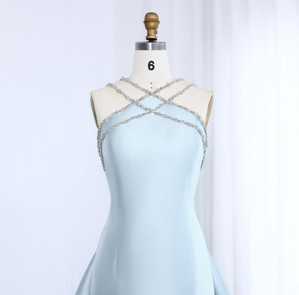Light blue satin evening gown with a crystal-beaded halter neckline and mermaid silhouette on a dress form.