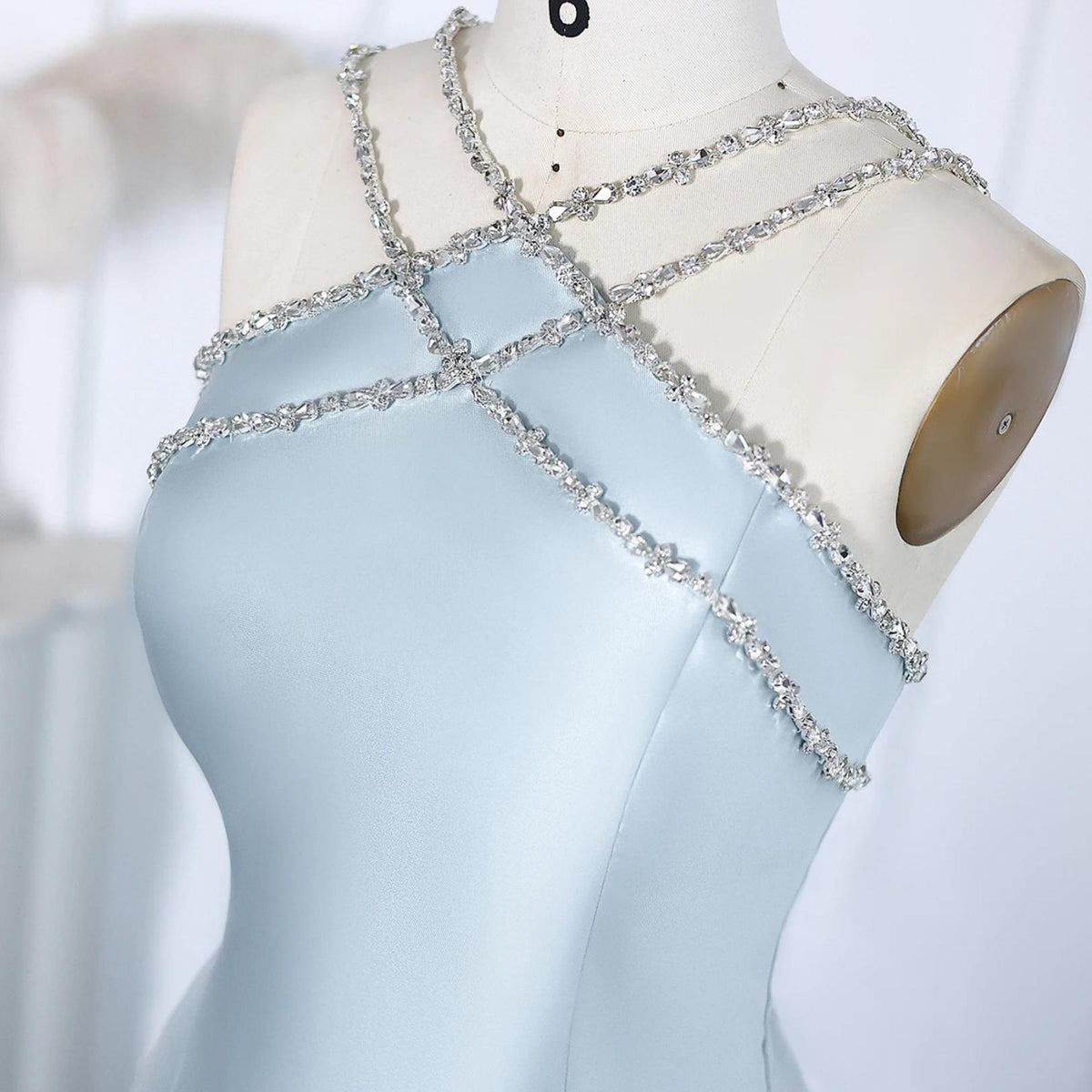 Light blue satin evening gown featuring a crystal-beaded halter neckline on a dressmaker's mannequin.