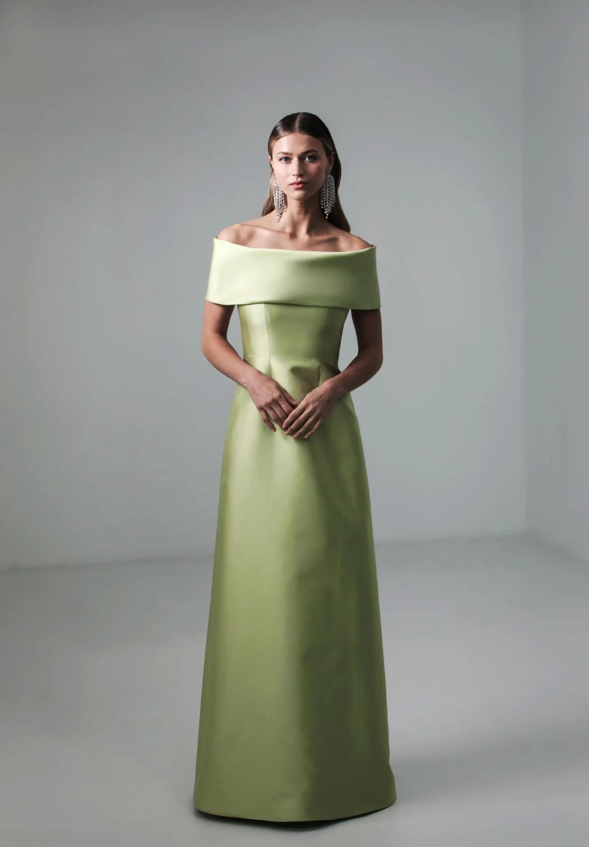 Model wearing a lime green silk A-line evening gown with an elegant off-shoulder neckline and fitted bodice.