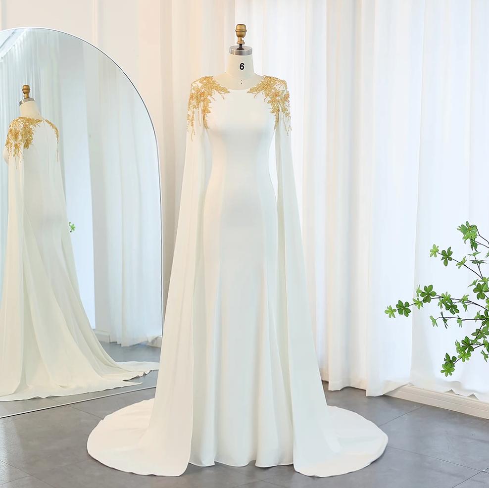 White mermaid gown with gold beaded shoulders, dramatic cape sleeves, and a floor-length sweep train on a mannequin.